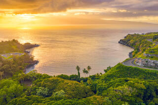 Aerial sunset view of lush green cliffs and coastal road framing Honolua Bay in Maui looking out toward Molokai island.