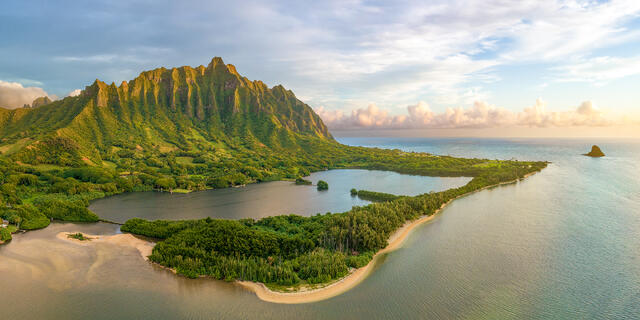Aerial view of historic Molii Fishpond in Kaneohe, Oahu with sunlit Koolau mountains, Kualoa Ranch, and Mokoli'i island.