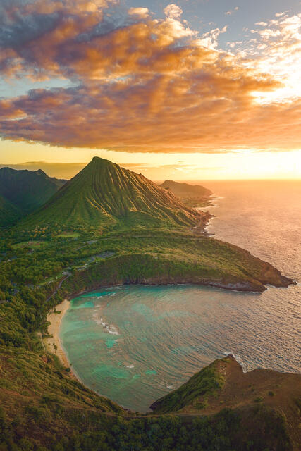 Aerial sunrise photo of Hanauma Bay in the foreground with Koko Head Crater rising under a golden cloud-filled sky on Oahu.