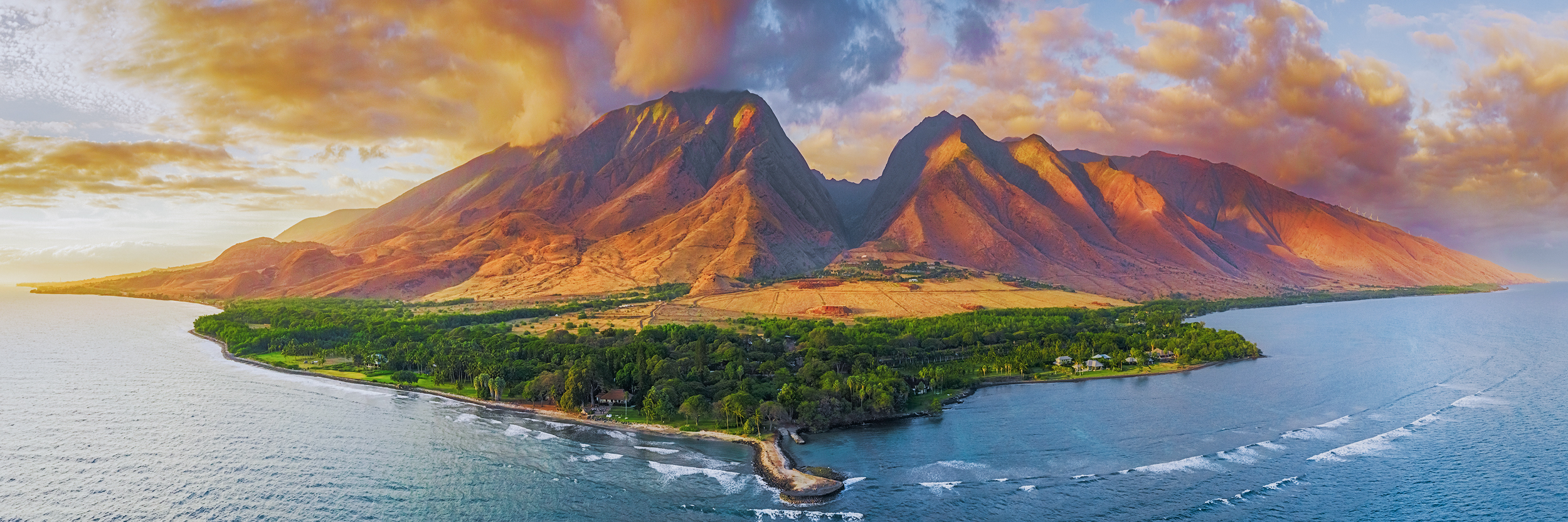 From The Mountain to the Sea A panoramic aerial photograph capturing the Olowalu coastline on Maui, showing a green tree-lined peninsula surrounded by blue ocean water.