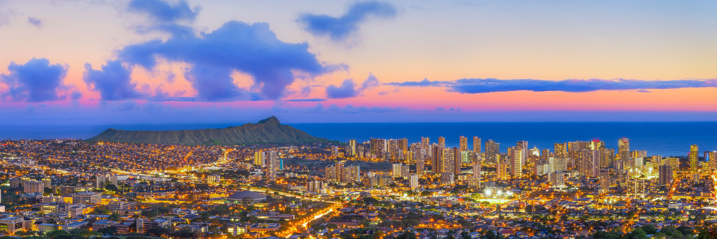 Honolulu City Lights Panoramic dusk view of twinkling Honolulu city lights and Waikiki skyline with Diamond Head crater under a colorful twilight sky.
