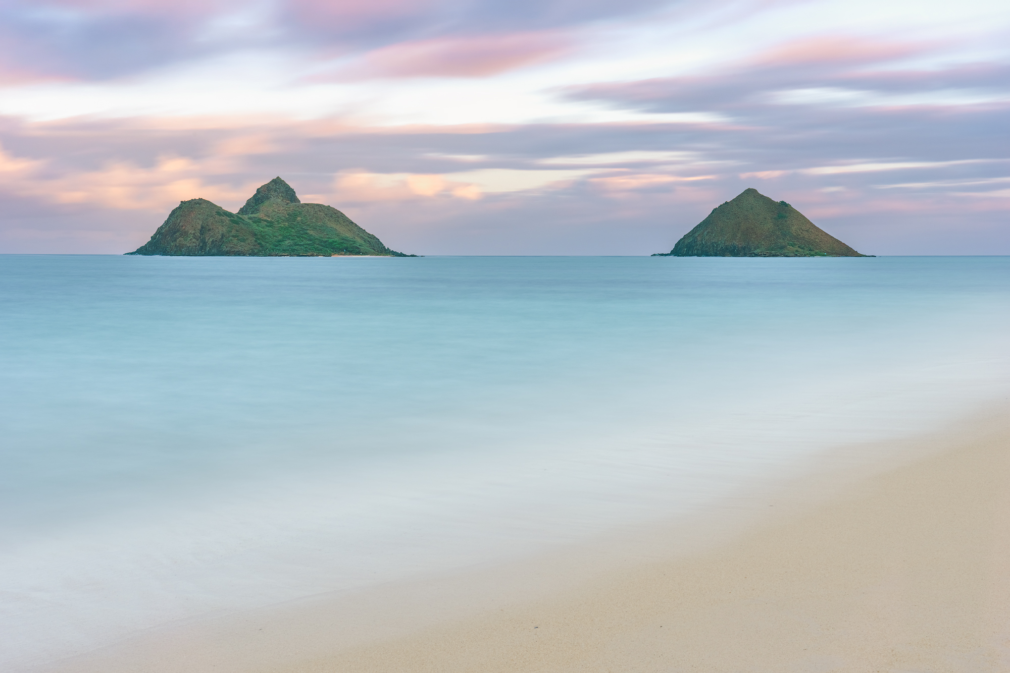 Guardians of Lanikai Long-exposure view of the Na Mokulua twin islands from Lanikai Beach on Oahu under a soft pastel sunset sky.