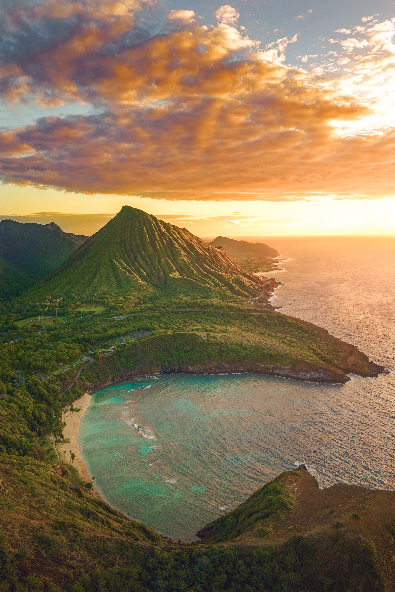 The Crater by the Bay Aerial sunrise photo of Hanauma Bay in the foreground with Koko Head Crater rising under a golden cloud-filled sky on Oahu.